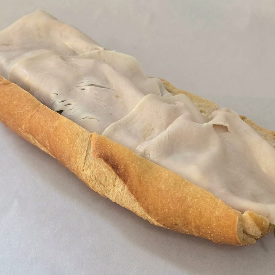 Long crusty sandwich roll filled with folded slices of pale deli meat on white paper.