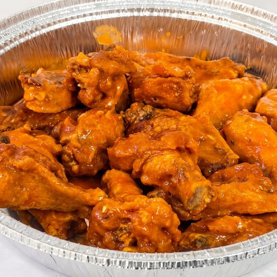 Aluminum tray filled with glossy orange-sauced chicken wings and drumettes.